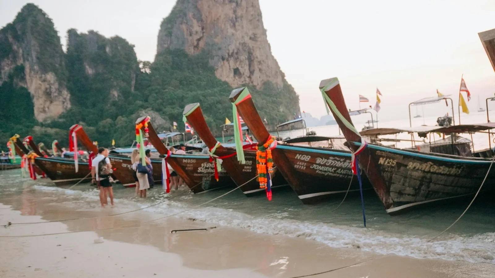 Longtailbåter på stranden under kalksteinsklippene i Krabi