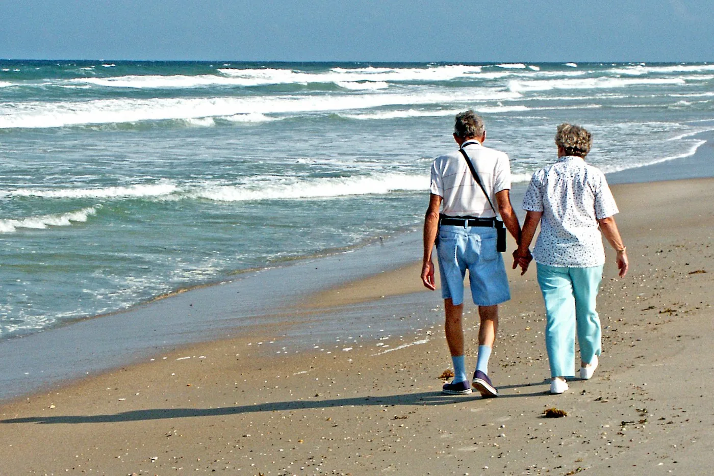 Eldre par som går hånd i hånd på stranden
